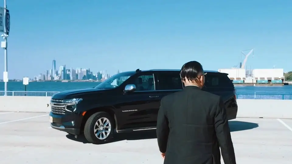 Black Chevrolet Suburban and chauffeur with the Manhattan skyline behind